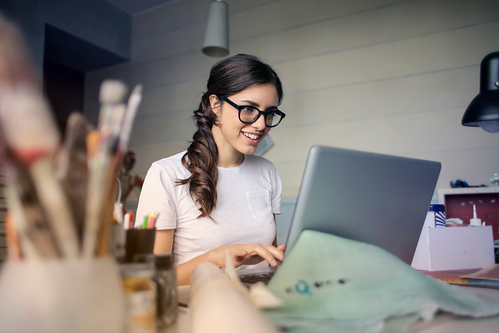 A woman smiling while sitting on a table using her laptop.